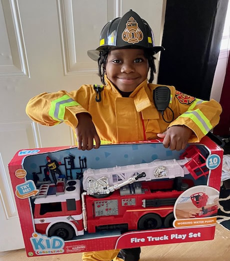 child wearing firefighter uniform and holding up boxed toy