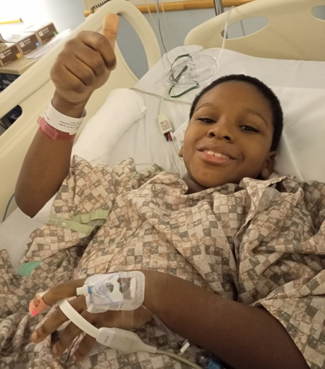 child in hospital bed holding up thumb